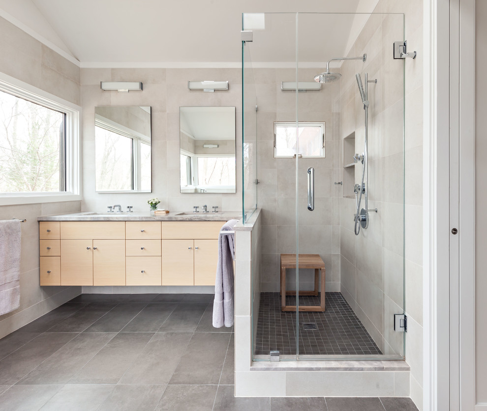 This is an example of a large contemporary master bathroom in New York with flat-panel cabinets, light wood cabinets, a freestanding tub, ceramic floors, a corner shower, beige tile, gray tile, ceramic tile, grey walls, an undermount sink, grey floor, a hinged shower door and grey benchtops.