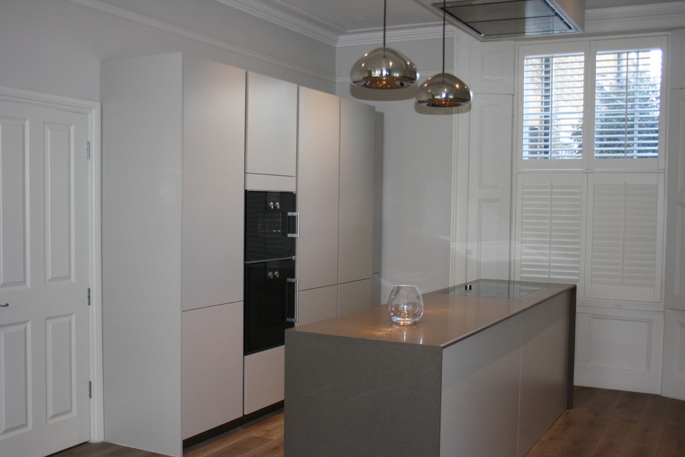 This is an example of a mid-sized contemporary galley eat-in kitchen in London with an undermount sink, flat-panel cabinets, grey cabinets, quartzite benchtops, grey splashback, stone slab splashback, black appliances, medium hardwood floors and with island.
