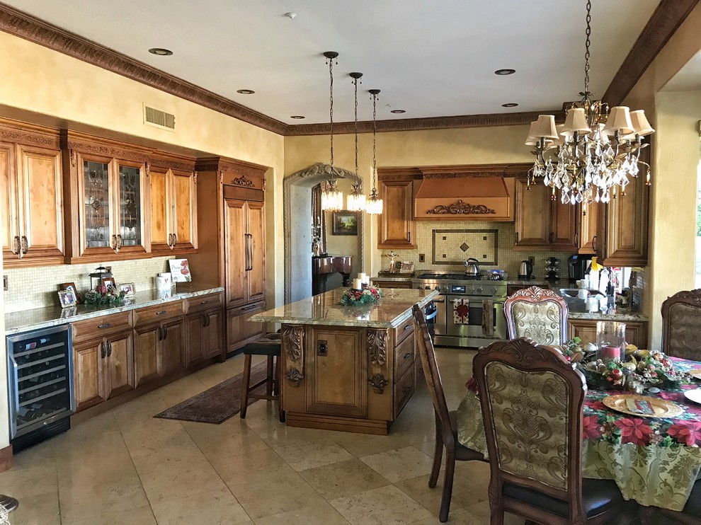 Design ideas for a large traditional l-shaped open plan kitchen in Phoenix with a farmhouse sink, raised-panel cabinets, medium wood cabinets, granite benchtops, beige splashback, travertine splashback, stainless steel appliances, travertine floors, with island, beige floor and beige benchtop.