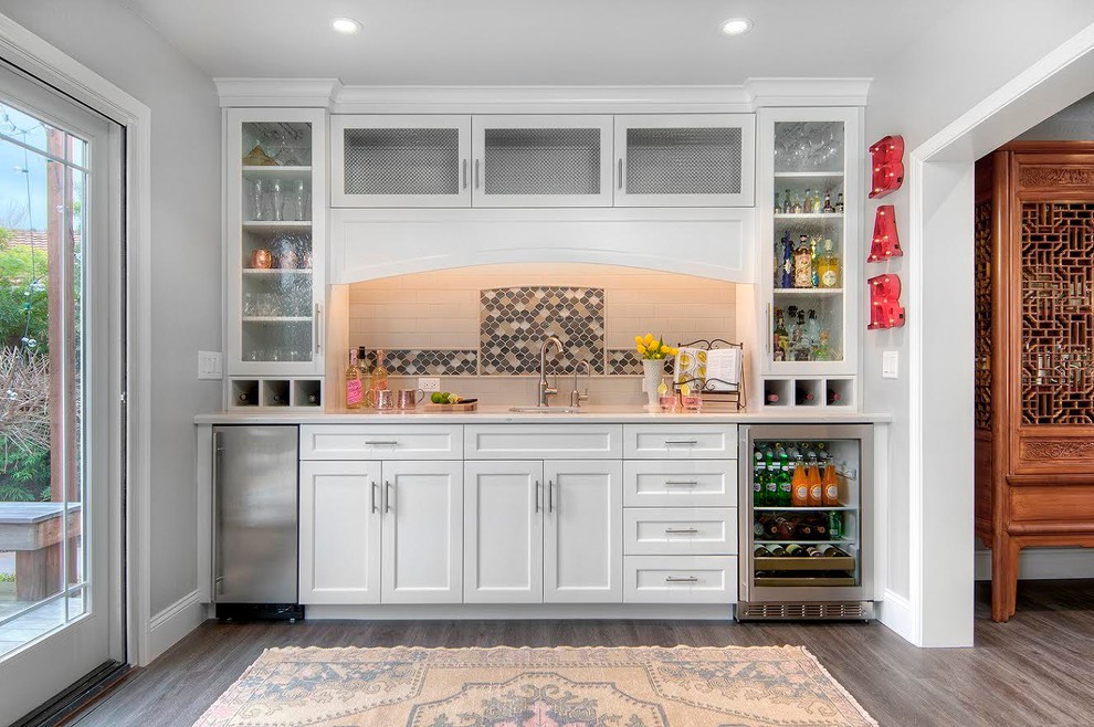 Photo of a small transitional single-wall wet bar in San Francisco with an undermount sink, white cabinets, white splashback, subway tile splashback, dark hardwood floors, brown floor, white benchtop and recessed-panel cabinets.