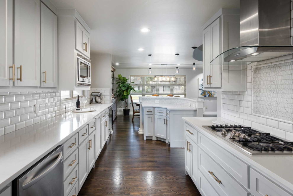 Inspiration for a medium sized classic grey and white galley kitchen/diner in Dallas with a submerged sink, shaker cabinets, white cabinets, engineered stone countertops, white splashback, metro tiled splashback, stainless steel appliances, dark hardwood flooring, a breakfast bar, brown floors and white worktops.