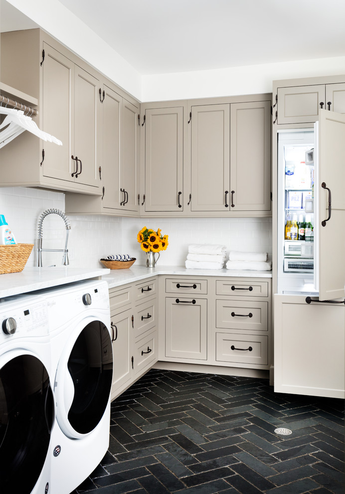 This is an example of a transitional l-shaped utility room in New York with white walls, slate floors, a side-by-side washer and dryer, white benchtop, shaker cabinets, beige cabinets and black floor.