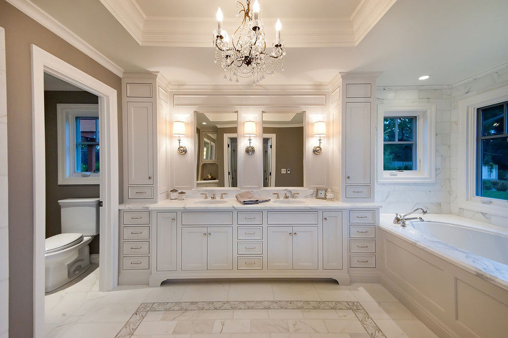 This is an example of a traditional master bathroom in San Francisco with an undermount sink, shaker cabinets, white cabinets, marble benchtops, an undermount tub, white tile, marble, white benchtops and an enclosed toilet.
