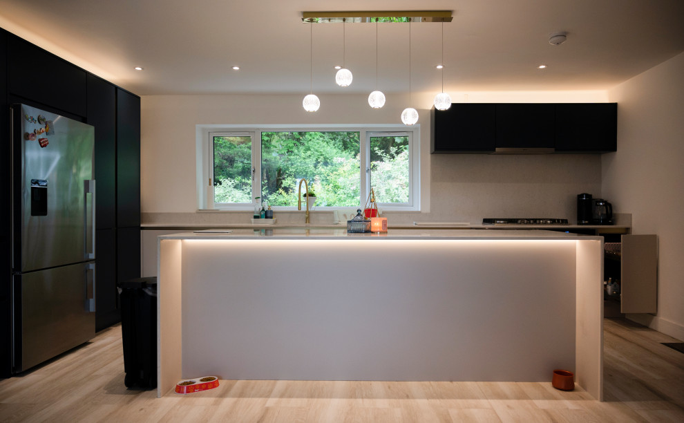This is an example of a mid-sized modern l-shaped eat-in kitchen in Manchester with an integrated sink, flat-panel cabinets, blue cabinets, solid surface benchtops, white splashback, engineered quartz splashback, black appliances, porcelain floors, with island, beige floor and beige benchtop.