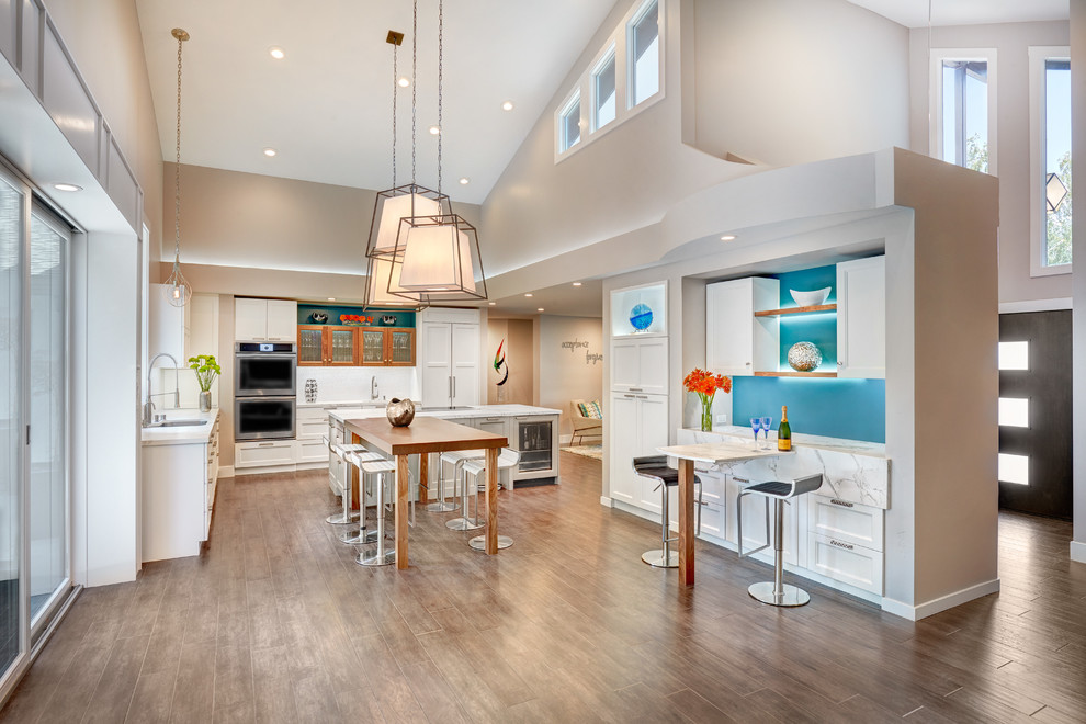 Photo of a mid-sized contemporary u-shaped open plan kitchen in Sacramento with an undermount sink, recessed-panel cabinets, white cabinets, quartz benchtops, white splashback, porcelain splashback, stainless steel appliances, medium hardwood floors and with island.