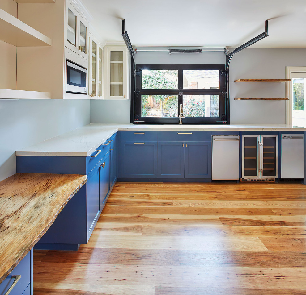 Example of a small transitional l-shaped medium tone wood floor open concept kitchen design in San Francisco with an undermount sink, shaker cabinets, blue cabinets, quartz countertops, stainless steel appliances, no island and white countertops