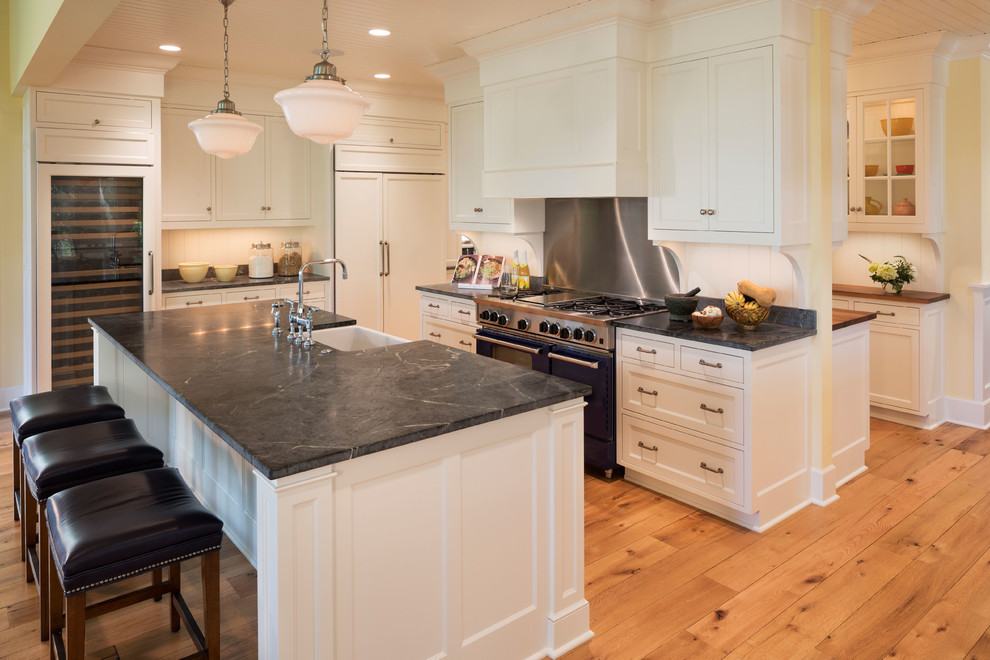 Traditional kitchen in Minneapolis with a farmhouse sink, recessed-panel cabinets, white cabinets, metallic splashback, stainless steel appliances, light hardwood floors and with island.