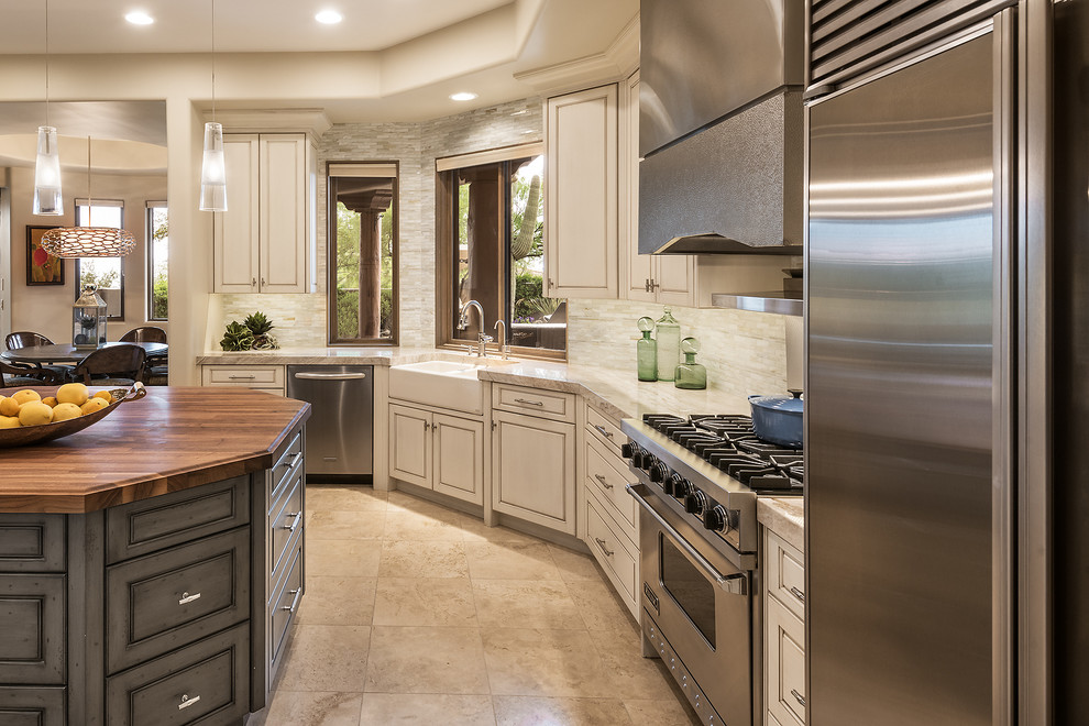 Mid-sized transitional kitchen in Phoenix with a farmhouse sink, flat-panel cabinets, beige cabinets, quartzite benchtops, white splashback, glass tile splashback, stainless steel appliances, travertine floors, with island and beige floor.
