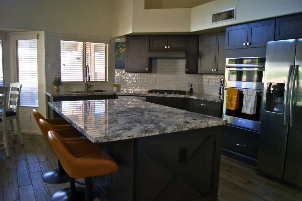 Mid-sized minimalist l-shaped porcelain tile and gray floor open concept kitchen photo in Phoenix with an undermount sink, shaker cabinets, brown cabinets, granite countertops, white backsplash, subway tile backsplash, stainless steel appliances, an island and white countertops