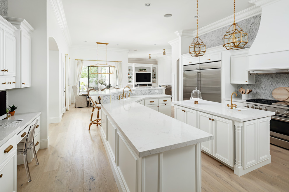 This is an example of a large traditional galley eat-in kitchen in Phoenix with an undermount sink, white cabinets, quartz benchtops, grey splashback, marble splashback, stainless steel appliances, light hardwood floors, multiple islands, beige floor, white benchtop and recessed-panel cabinets.