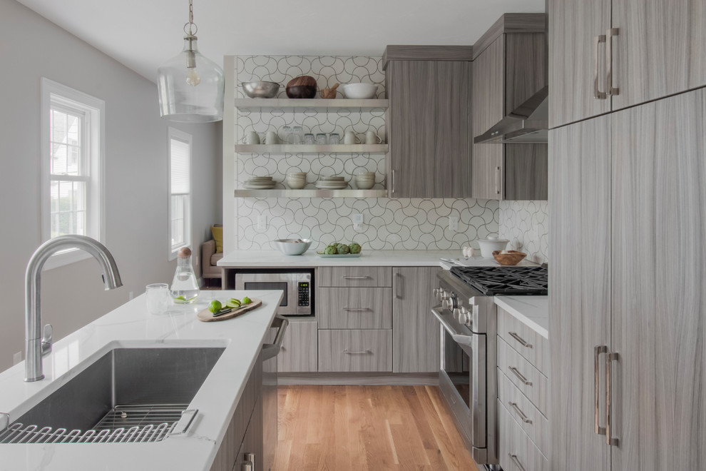 This is an example of a contemporary l-shaped kitchen in Boston with an undermount sink, flat-panel cabinets, grey cabinets, white splashback, panelled appliances, medium hardwood floors, with island and brown floor.