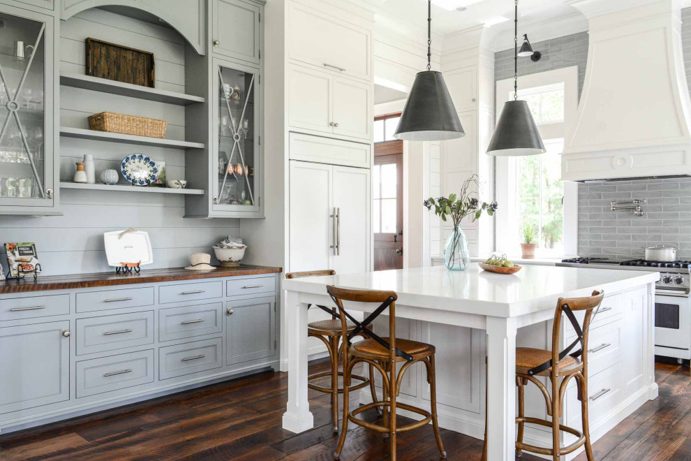 Design ideas for a traditional kitchen with a belfast sink, shaker cabinets, grey cabinets, wood worktops, grey splashback, glass tiled splashback, stainless steel appliances, an island and brown worktops.