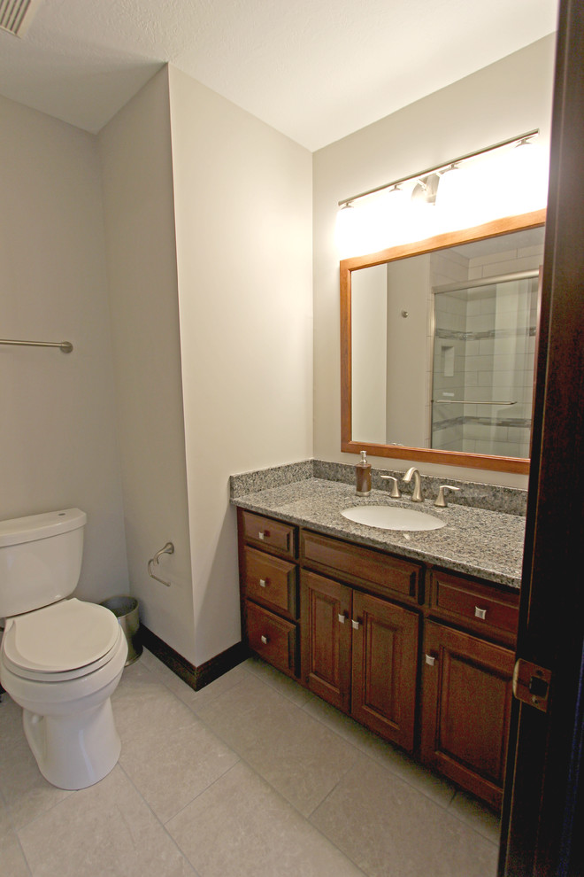 This is an example of a small traditional kids bathroom in Cleveland with an undermount sink, dark wood cabinets, granite benchtops, an alcove shower, beige tile, beige walls and porcelain floors.