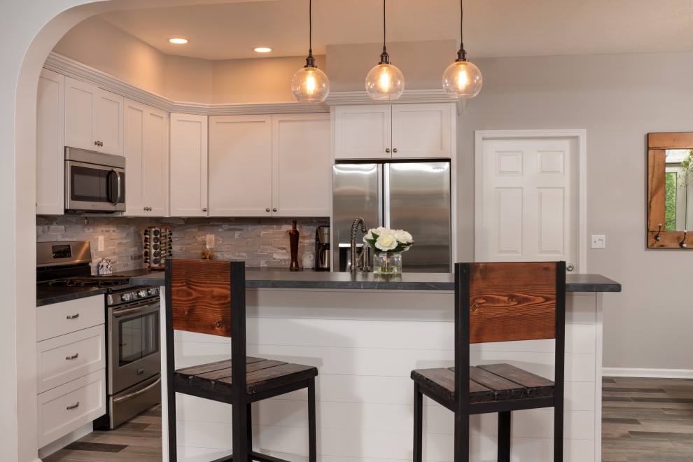 Open concept kitchen - mid-sized rustic l-shaped porcelain tile and gray floor open concept kitchen idea with an undermount sink, shaker cabinets, white cabinets, granite countertops, gray backsplash, brick backsplash, stainless steel appliances, an island and black countertops