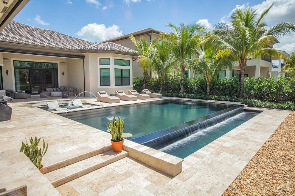 Large modern backyard rectangular infinity pool in Miami with a hot tub and natural stone pavers.