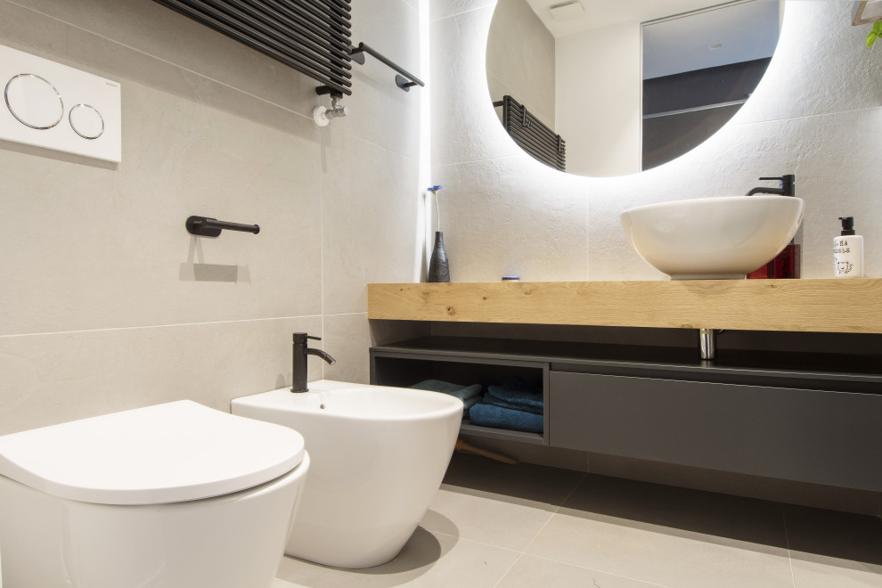 Small contemporary cloakroom in Turin with flat-panel cabinets, grey cabinets, a two-piece toilet, grey tiles, porcelain tiles, white walls, porcelain flooring, a vessel sink, wooden worktops, grey floors, brown worktops, a floating vanity unit and a drop ceiling.