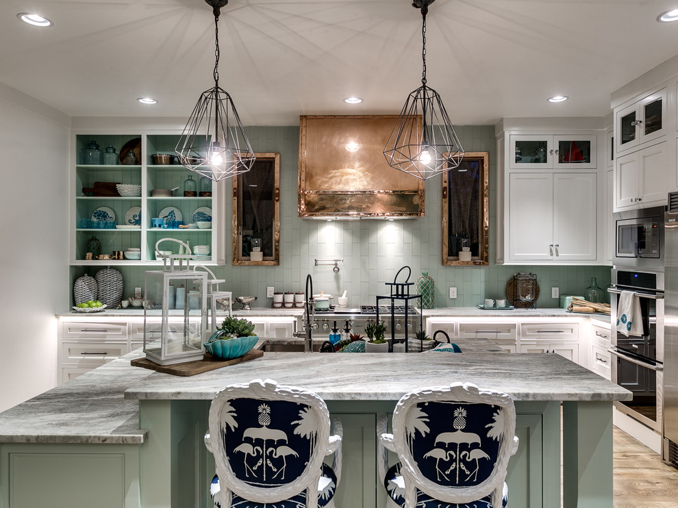 Photo of a beach style l-shaped eat-in kitchen in Oklahoma City with an undermount sink, beaded inset cabinets, white cabinets, green splashback, stainless steel appliances, light hardwood floors and with island.