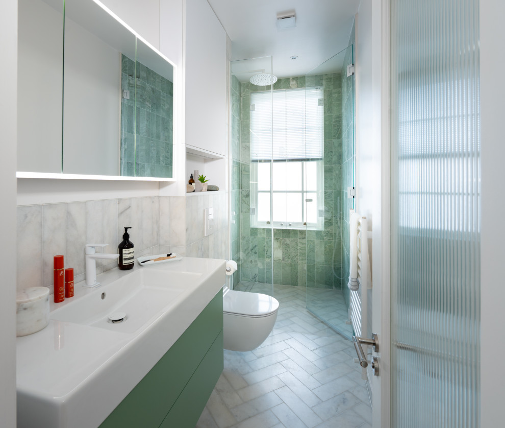 This is an example of a medium sized contemporary bathroom in London with flat-panel cabinets, green cabinets, a wall mounted toilet, green tiles, marble tiles, white walls, marble flooring, a wall-mounted sink, white floors, a hinged door, a wall niche, a single sink and a floating vanity unit.