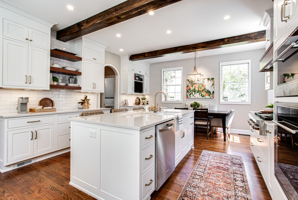 Large transitional u-shaped separate kitchen in Atlanta with an undermount sink, beaded inset cabinets, white cabinets, quartz benchtops, white splashback, subway tile splashback, stainless steel appliances, medium hardwood floors, with island, brown floor, grey benchtop and exposed beam.