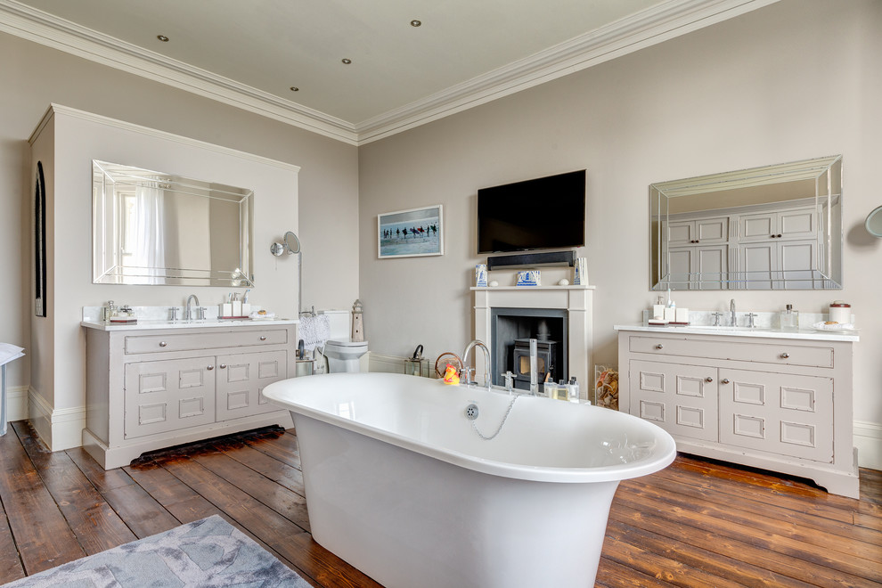 Photo of an expansive transitional master bathroom in Devon with furniture-like cabinets, grey cabinets, granite benchtops, a freestanding tub, an alcove shower, a one-piece toilet, white tile, ceramic tile and medium hardwood floors.