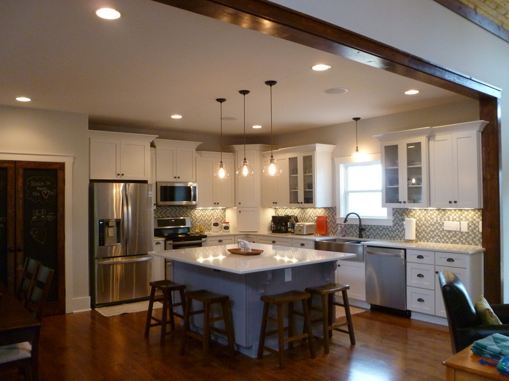 Inspiration for a mid-sized arts and crafts l-shaped eat-in kitchen in Nashville with a farmhouse sink, shaker cabinets, white cabinets, grey splashback, glass tile splashback, stainless steel appliances, medium hardwood floors and with island.
