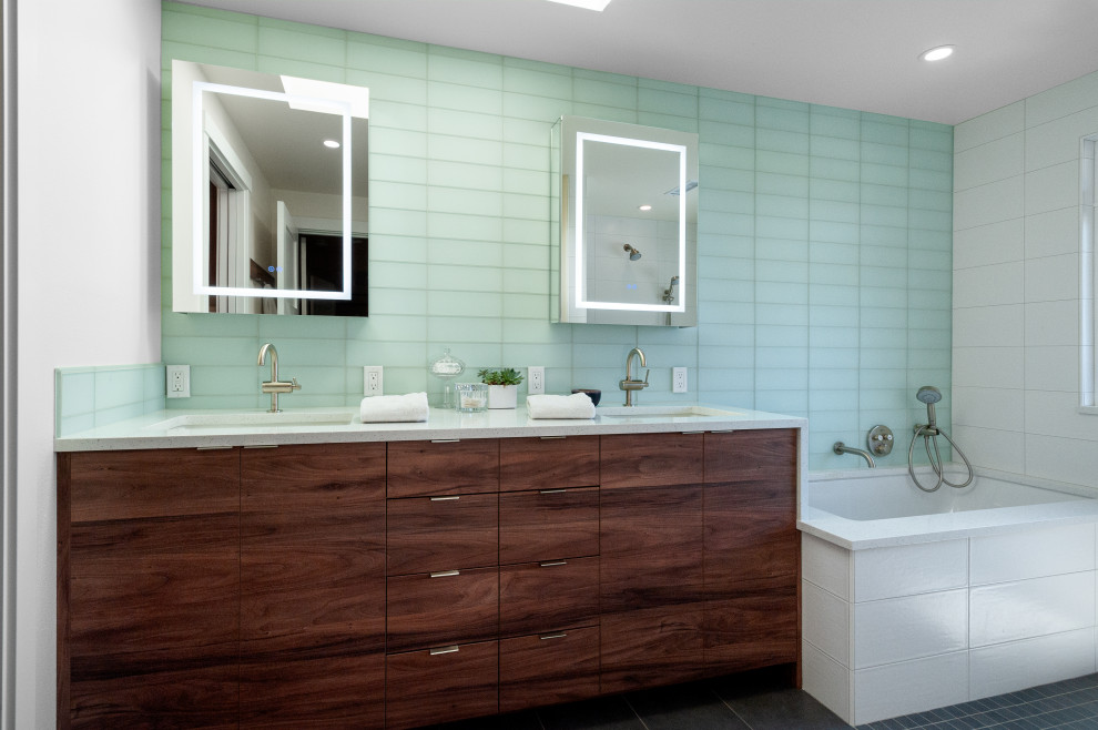 На фото: главная ванная комната среднего размера со стиральной машиной в современном стиле с плоскими фасадами, темными деревянными фасадами, полновстраиваемой ванной, открытым душем, зеленой плиткой, стеклянной плиткой, белыми стенами, полом из керамогранита, врезной раковиной, столешницей из искусственного кварца, серым полом, открытым душем, бежевой столешницей, тумбой под две раковины и встроенной тумбой с