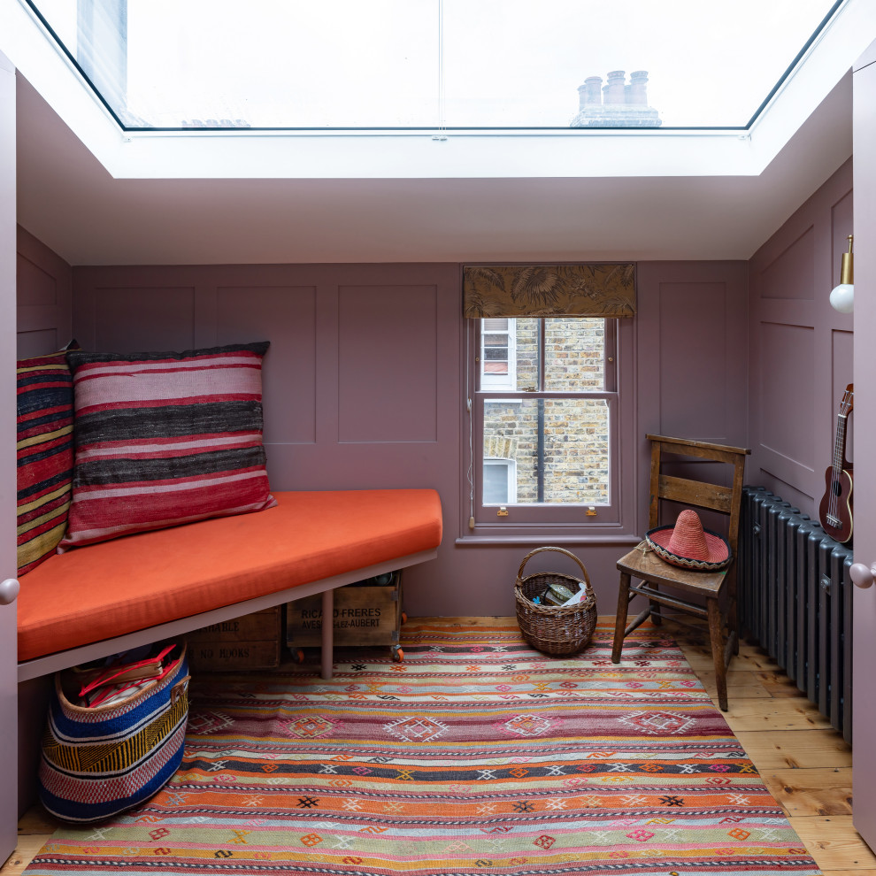 На фото: открытая гостиная комната среднего размера в стиле фьюжн с с книжными шкафами и полками, розовыми стенами, паркетным полом среднего тона, скрытым телевизором и панелями на части стены с