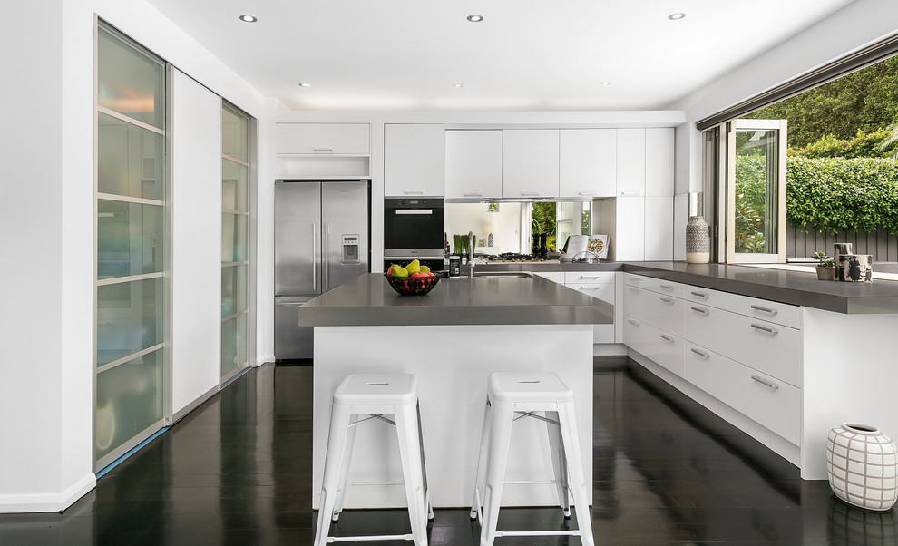 Large contemporary l-shaped kitchen pantry in Sydney with a double-bowl sink, white cabinets, concrete benchtops, mirror splashback, stainless steel appliances, dark hardwood floors, with island, brown floor and flat-panel cabinets.