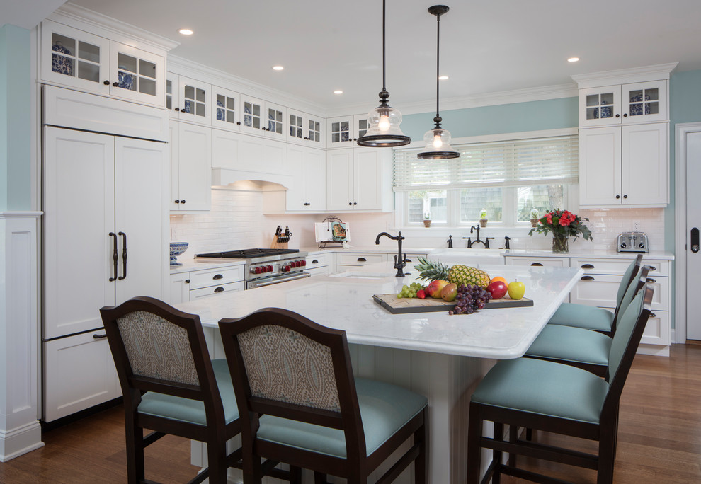 Inspiration for a large transitional galley medium tone wood floor and brown floor eat-in kitchen remodel with a farmhouse sink, recessed-panel cabinets, white cabinets, quartz countertops, white backsplash, subway tile backsplash, paneled appliances and an island