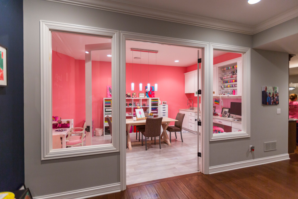 This is an example of a large modern craft room in Cincinnati with pink walls, ceramic floors, a built-in desk and grey floor.