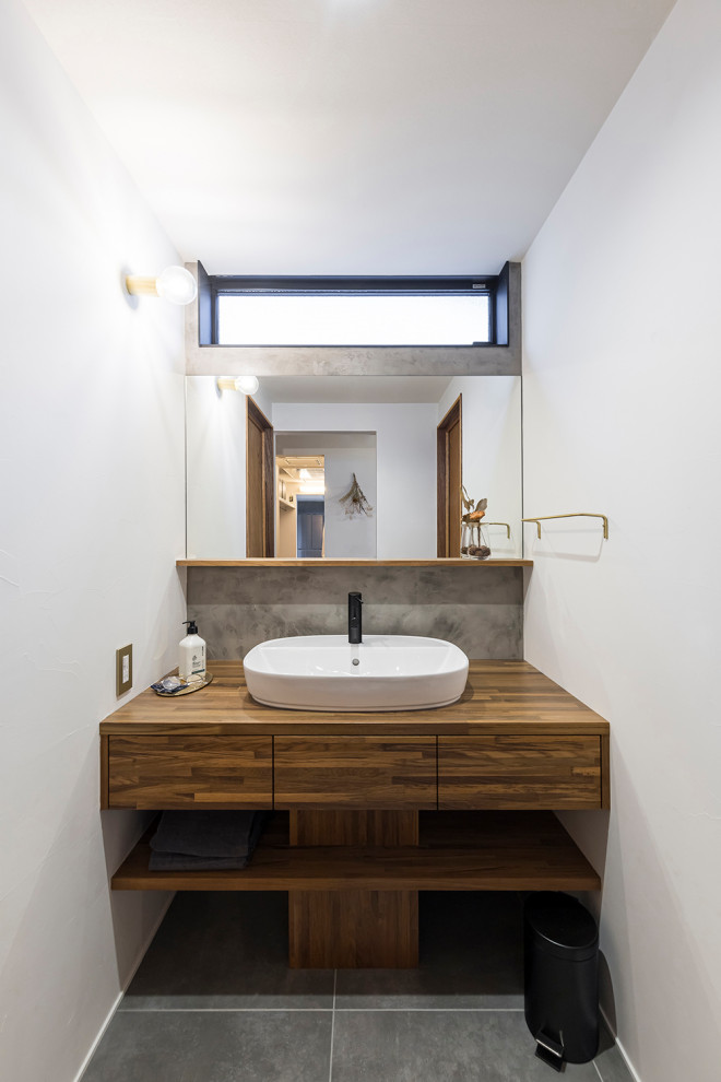 Foto på ett 50 tals brun toalett, med luckor med profilerade fronter, skåp i mörkt trä, grå kakel, grå väggar, vinylgolv, ett fristående handfat, träbänkskiva och grått golv