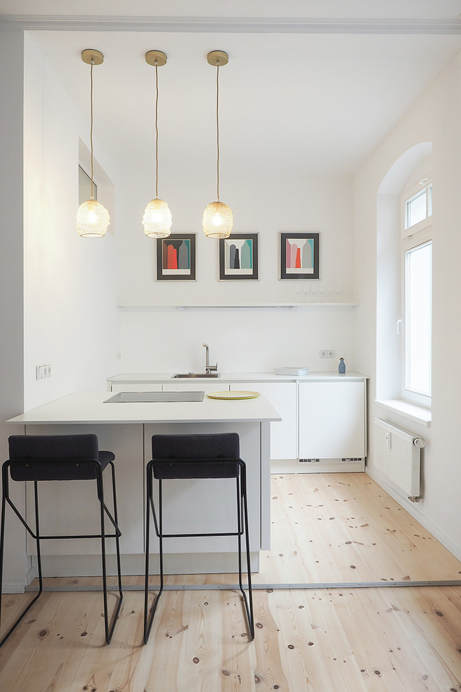 This is an example of a small midcentury u-shaped open plan kitchen in Berlin with a drop-in sink, flat-panel cabinets, white cabinets, light hardwood floors, a peninsula and brown floor.