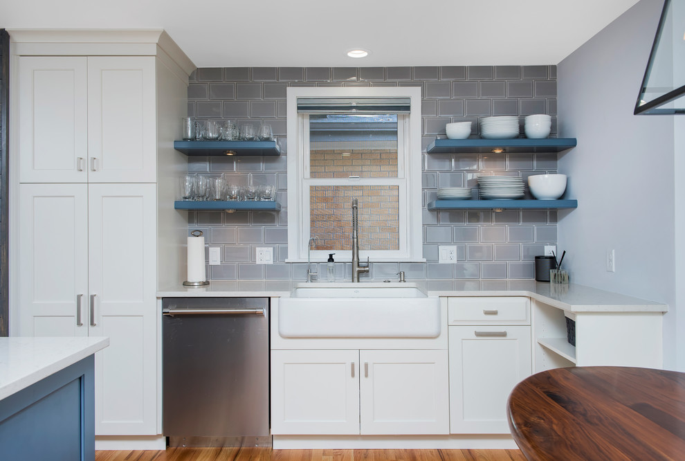 Large transitional u-shaped light wood floor enclosed kitchen photo in Denver with a farmhouse sink, shaker cabinets, white cabinets, quartz countertops, gray backsplash, ceramic backsplash, stainless steel appliances and an island