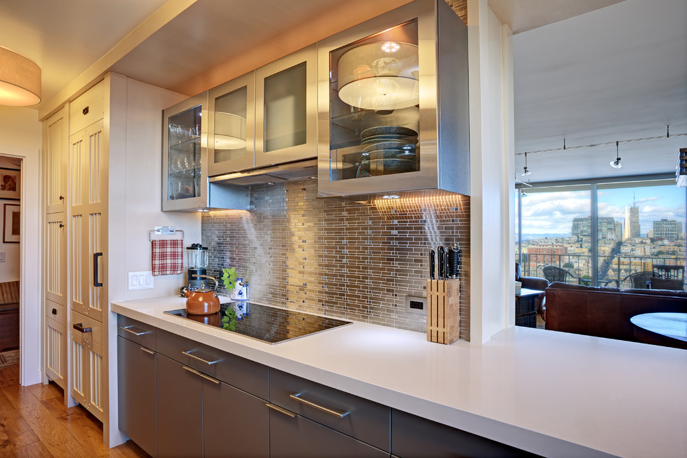 This is an example of a mid-sized contemporary galley separate kitchen in San Francisco with an undermount sink, flat-panel cabinets, beige cabinets, solid surface benchtops, metallic splashback, metal splashback, panelled appliances, medium hardwood floors, a peninsula and yellow floor.