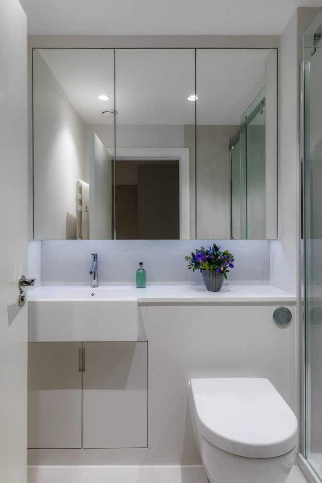 Photo of a mid-sized contemporary master bathroom in London with flat-panel cabinets, a curbless shower, a wall-mount toilet, white walls, porcelain floors, an integrated sink, solid surface benchtops, white floor, a sliding shower screen, white benchtops, a built-in vanity, grey cabinets and a single vanity.