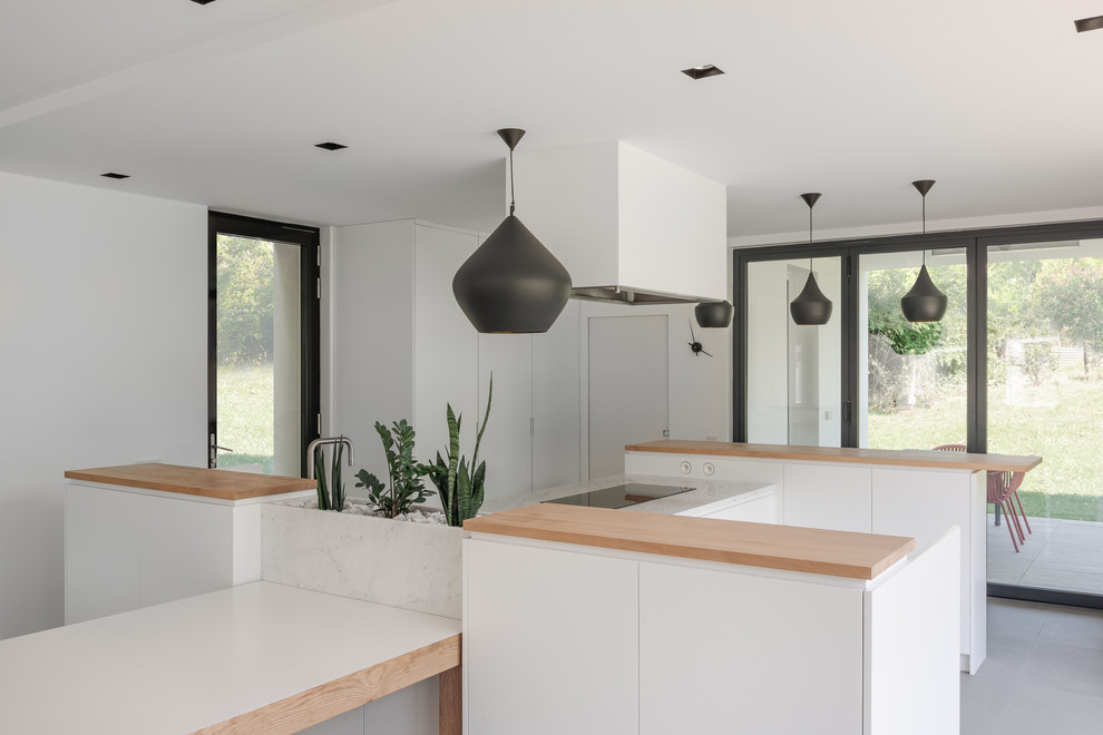 Photo of a scandinavian open plan kitchen with flat-panel cabinets, white cabinets, stainless steel appliances, grey floor, an integrated sink, marble benchtops, white splashback, marble splashback, multiple islands and white benchtop.