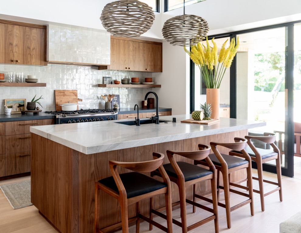 Design ideas for a mid-sized contemporary galley kitchen in Orange County with an undermount sink, flat-panel cabinets, medium wood cabinets, white splashback, glass tile splashback, black appliances, light hardwood floors, with island, beige floor and brown benchtop.