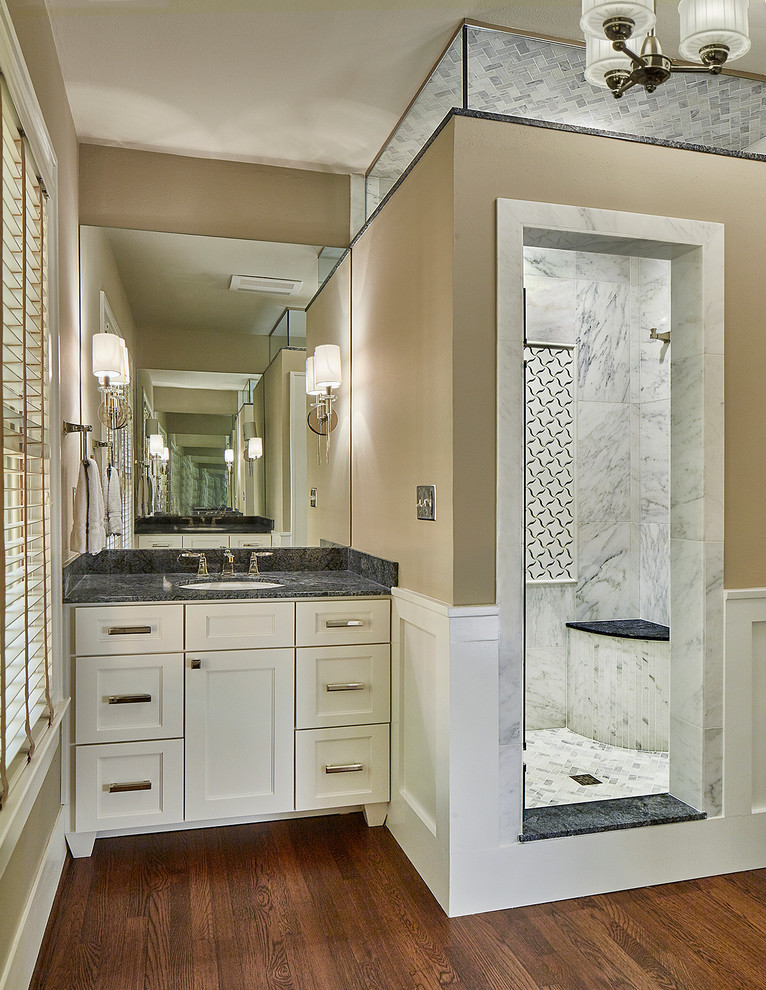 This is an example of a mid-sized traditional master bathroom in Dallas with an undermount sink, shaker cabinets, white cabinets, marble benchtops, a corner shower, a two-piece toilet, white tile, stone tile, beige walls, medium hardwood floors, brown floor, a hinged shower door, grey benchtops, a single vanity and a built-in vanity.