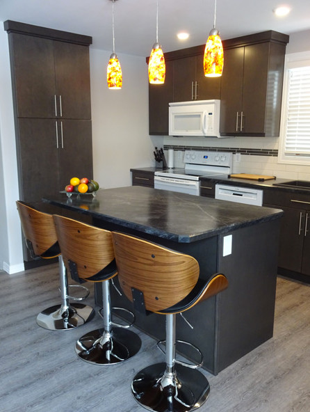 Open concept kitchen - mid-sized contemporary u-shaped open concept kitchen idea with a double-bowl sink, flat-panel cabinets, black cabinets, soapstone countertops, white backsplash, subway tile backsplash, white appliances and an island