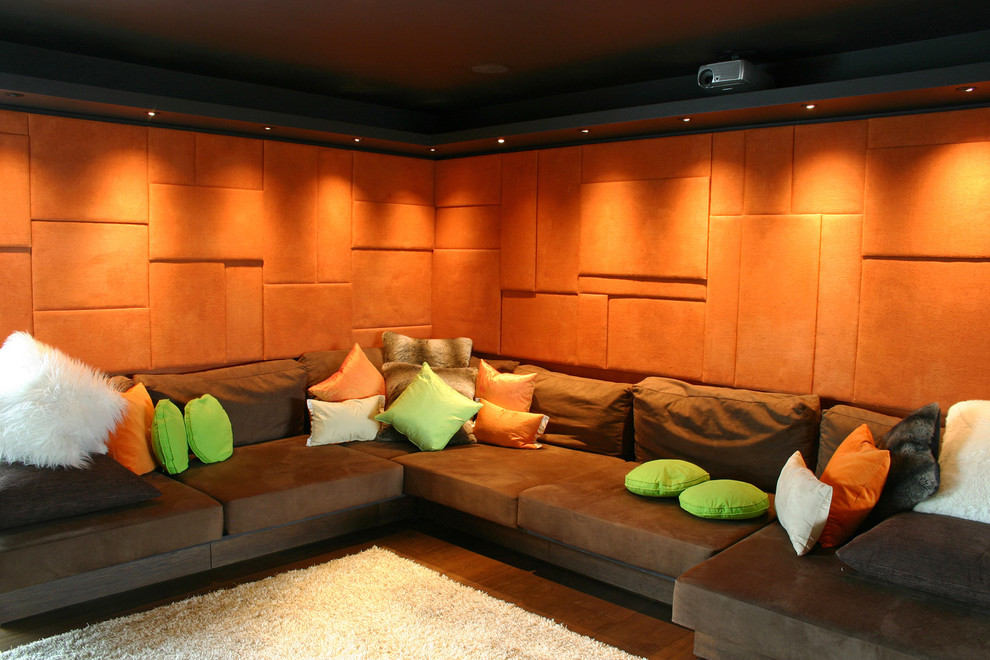 Photo of a mid-sized modern enclosed home theatre in London with orange walls, dark hardwood floors and a projector screen.