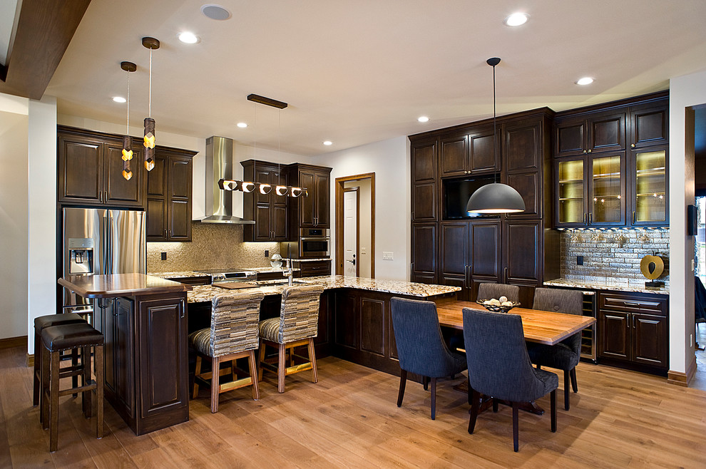 Example of a large transitional l-shaped light wood floor and brown floor eat-in kitchen design with an undermount sink, raised-panel cabinets, dark wood cabinets, granite countertops, multicolored backsplash, mosaic tile backsplash, stainless steel appliances and two islands