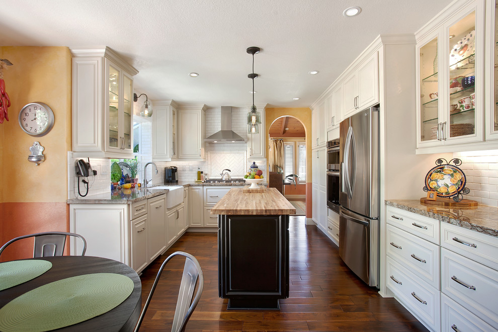 Inspiration for a large traditional u-shaped eat-in kitchen in San Diego with a farmhouse sink, raised-panel cabinets, white cabinets, granite benchtops, white splashback, subway tile splashback, stainless steel appliances, medium hardwood floors and with island.