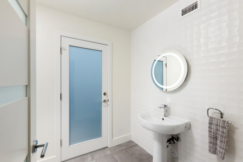This is an example of a mid-sized modern 3/4 bathroom in Orange County with glass-front cabinets, white cabinets, a two-piece toilet, white tile, ceramic tile, white walls, porcelain floors, a pedestal sink, grey floor, a single vanity and a freestanding vanity.