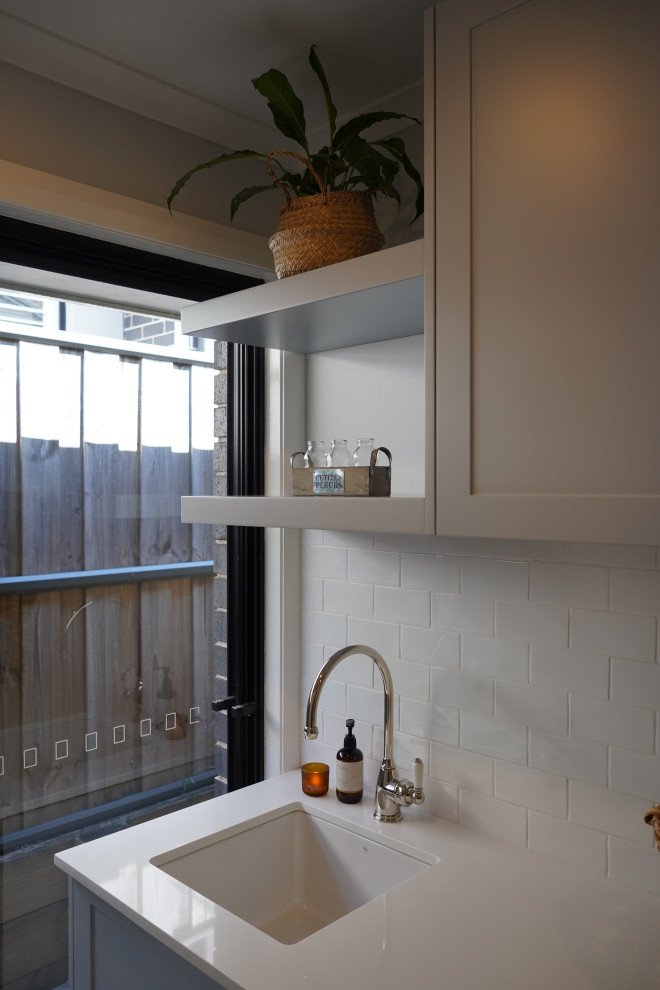 Idéer för små linjära vitt tvättstugor enbart för tvätt, med en undermonterad diskho, skåp i shakerstil, grå skåp, bänkskiva i kvarts, vitt stänkskydd, stänkskydd i tunnelbanekakel, vita väggar, marmorgolv, en tvättmaskin och torktumlare bredvid varandra och grått golv