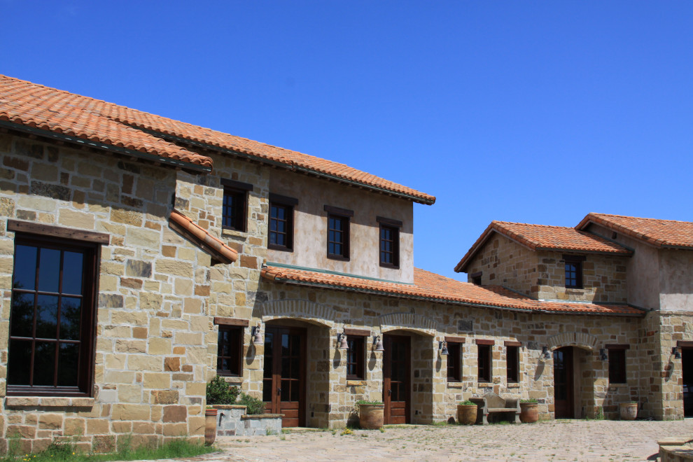 На фото: большой, двухэтажный частный загородный дом в средиземноморском стиле с облицовкой из камня, двускатной крышей, черепичной крышей и красной крышей