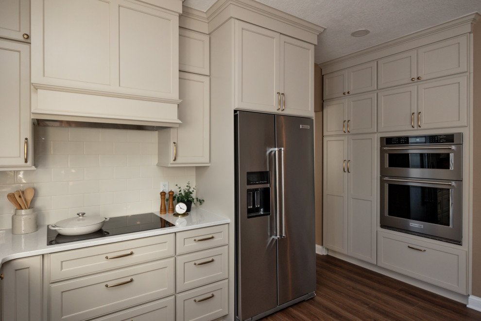 Example of a large transitional u-shaped dark wood floor and brown floor open concept kitchen design with an undermount sink, recessed-panel cabinets, beige cabinets, quartz countertops, white backsplash, subway tile backsplash, stainless steel appliances, a peninsula and white countertops