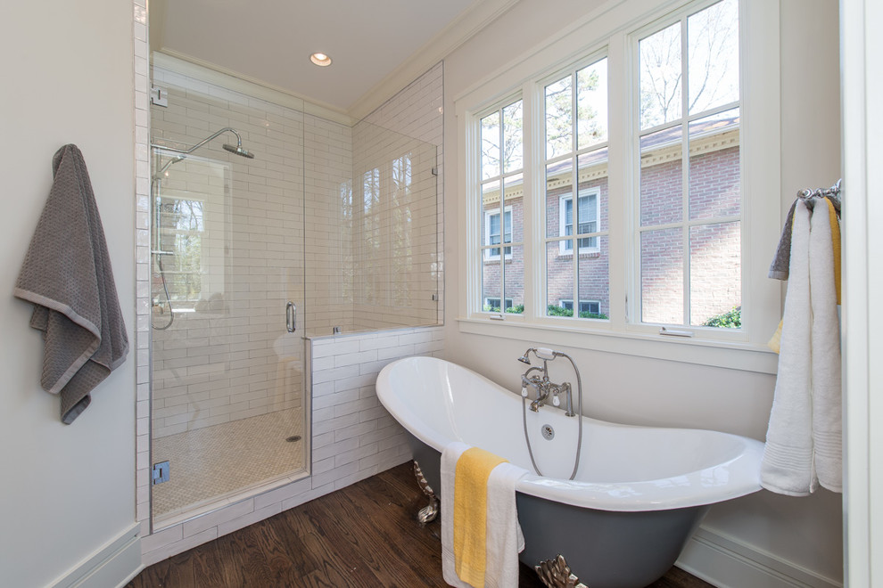 This is an example of a mid-sized traditional master bathroom in Charlotte with a claw-foot tub, white tile, white walls, medium hardwood floors, brown floor and a hinged shower door.