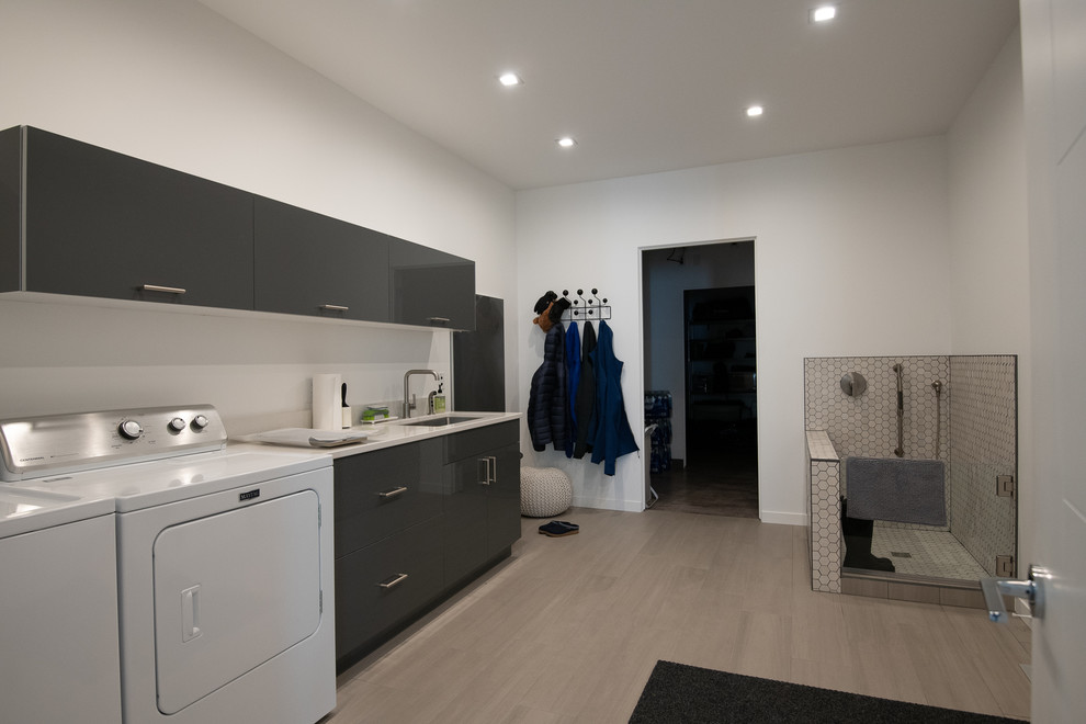 Photo of a mid-sized contemporary single-wall dedicated laundry room in Other with an undermount sink, flat-panel cabinets, grey cabinets, quartzite benchtops, white walls, porcelain floors, a side-by-side washer and dryer, beige floor and white benchtop.