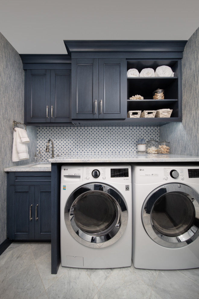 Small transitional galley dedicated laundry room in Other with blue cabinets, a side-by-side washer and dryer, grey benchtop, wallpaper, a drop-in sink, beaded inset cabinets, marble benchtops, multi-coloured splashback, porcelain splashback, blue walls, marble floors and white floor.