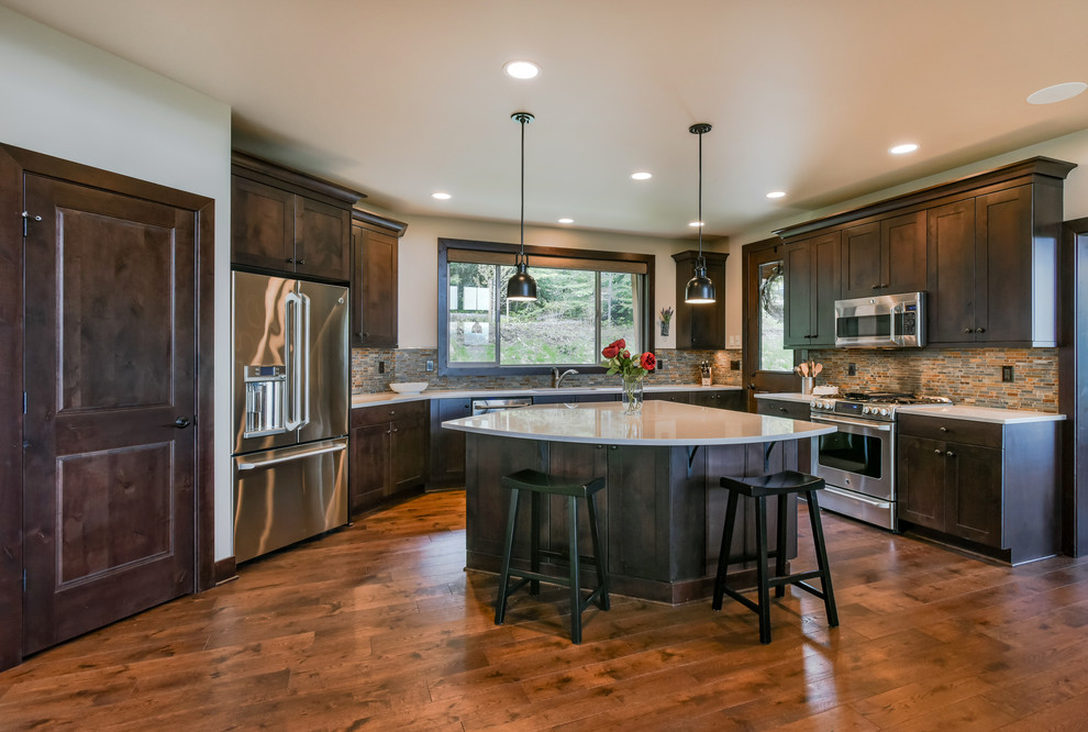 Mountain style l-shaped medium tone wood floor and brown floor kitchen photo in Seattle with shaker cabinets, dark wood cabinets, multicolored backsplash, stainless steel appliances, an island and beige countertops